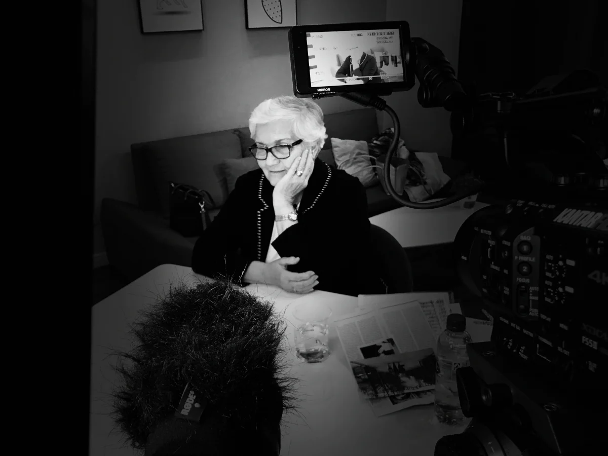 Interviewpartnerin am Tisch mit Fotos und Mikrofon, in Schwarz-Weiß